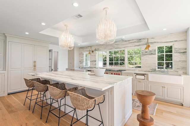 kitchen with a sink, a breakfast bar, a raised ceiling, a center island, and a notable chandelier