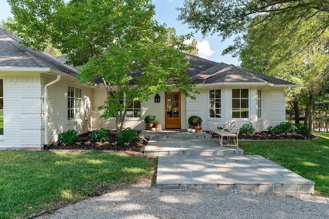view of front of property with roof with shingles, a front yard, and brick siding