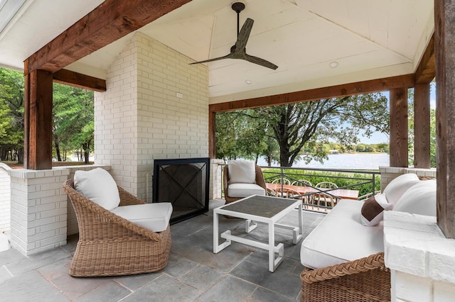 view of patio featuring a ceiling fan, a water view, and an outdoor living space with a fireplace