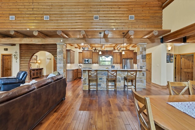 living area with decorative columns, arched walkways, beamed ceiling, and dark wood finished floors