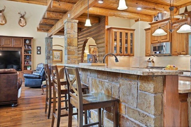 kitchen with stainless steel microwave, log walls, light stone counters, wood ceiling, and hardwood / wood-style flooring