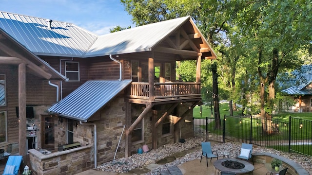 back of property featuring a patio, stone siding, metal roof, an outdoor fire pit, and fence