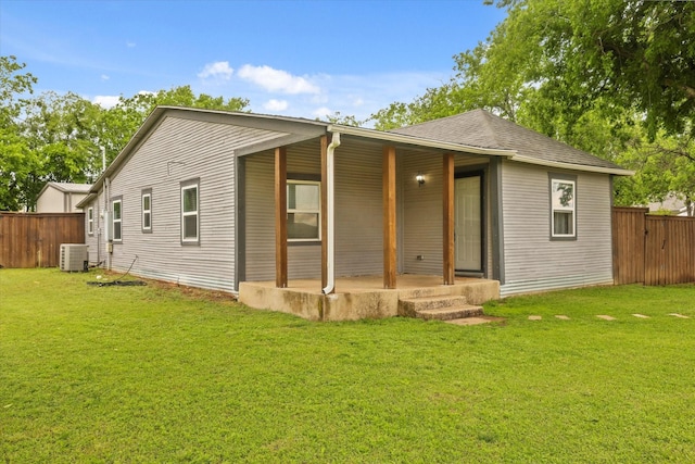 back of house featuring fence, a shingled roof, covered porch, central air condition unit, and a lawn