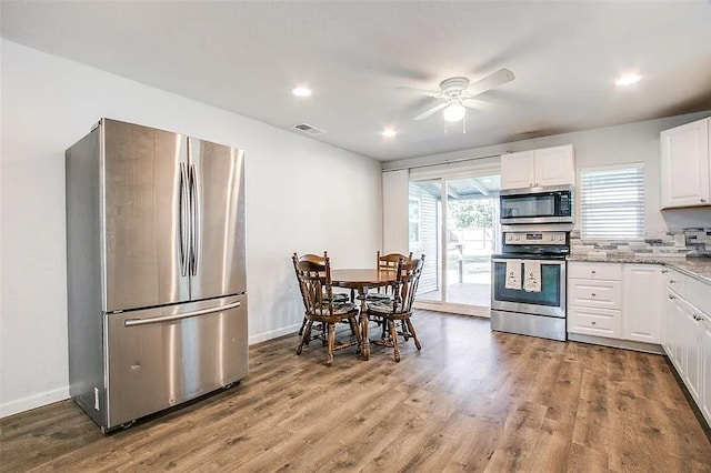 kitchen with wood finished floors, appliances with stainless steel finishes, white cabinetry, visible vents, and a ceiling fan