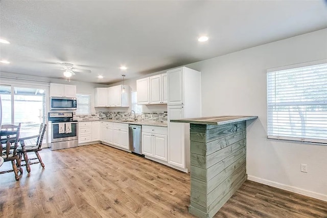 kitchen featuring white cabinetry, light wood-style flooring, stainless steel appliances, light countertops, and baseboards