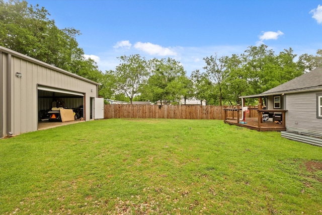 view of yard with a garage, a fenced backyard, a wooden deck, and an outbuilding