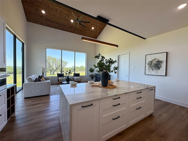 kitchen with high vaulted ceiling, light stone counters, white cabinets, open floor plan, and dark wood finished floors