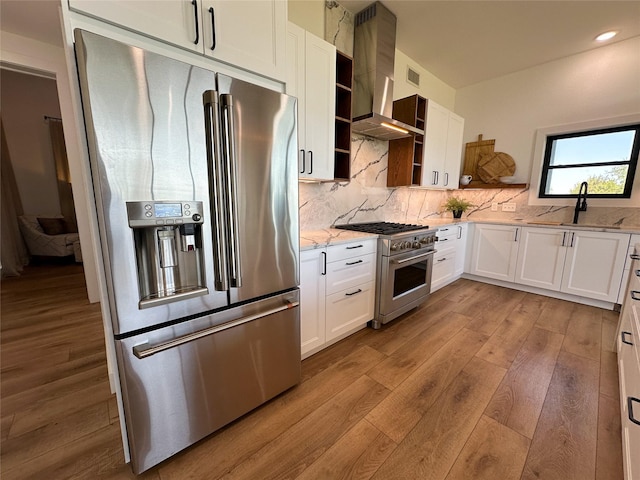 kitchen featuring wall chimney range hood, open shelves, a sink, light wood-style floors, and high end appliances