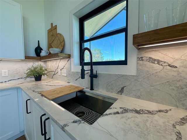 interior details with white cabinetry, a sink, light stone counters, and tasteful backsplash
