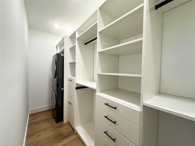 spacious closet with stacked washer and clothes dryer and light wood-type flooring