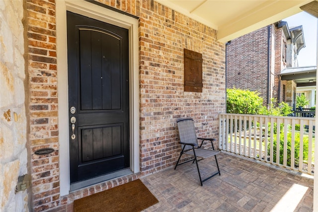 entrance to property featuring covered porch and brick siding
