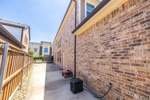 view of side of home with a patio, brick siding, and fence