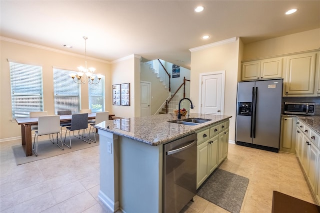kitchen with light stone counters, a sink, stainless steel appliances, an inviting chandelier, and a center island with sink