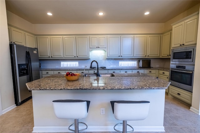 kitchen with a sink, appliances with stainless steel finishes, a breakfast bar, stone countertops, and a kitchen island with sink