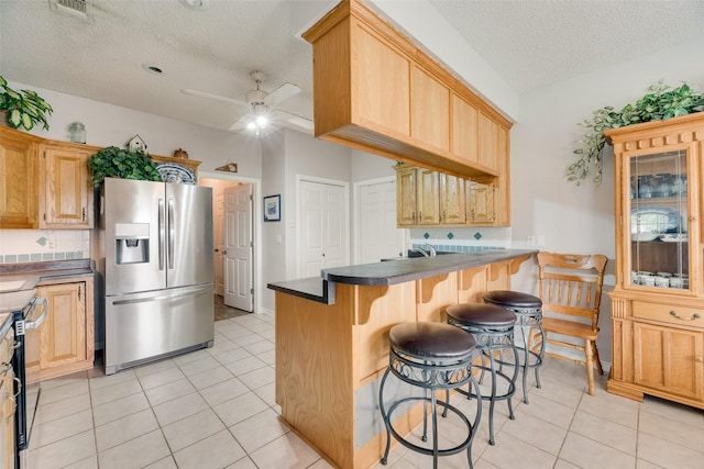 kitchen featuring dark countertops, stainless steel fridge with ice dispenser, a breakfast bar area, a textured ceiling, and a peninsula