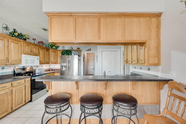 kitchen with dark countertops, a kitchen breakfast bar, stainless steel appliances, and a peninsula
