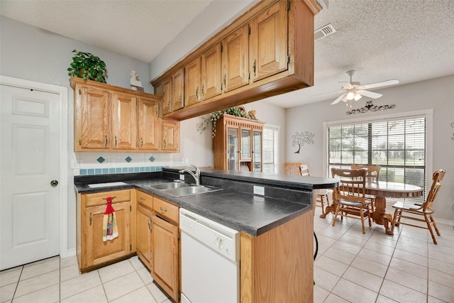 kitchen with white dishwasher, dark countertops, a peninsula, and a sink