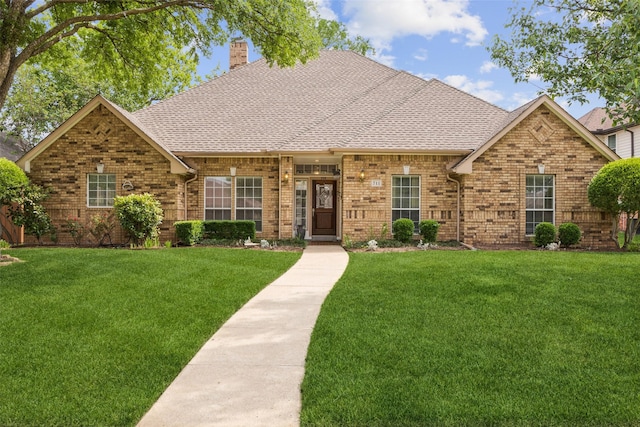 view of front of property with brick siding, a chimney, roof with shingles, and a front lawn