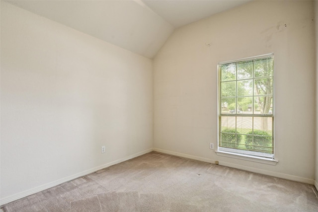 empty room with baseboards, vaulted ceiling, and light carpet