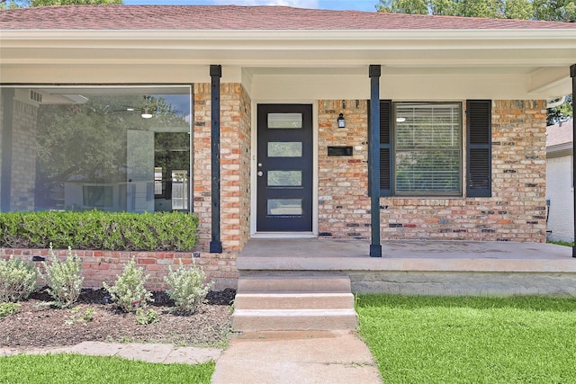 doorway to property with covered porch, brick siding, and roof with shingles