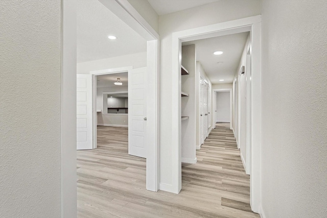 corridor featuring baseboards, light wood finished floors, and a textured wall