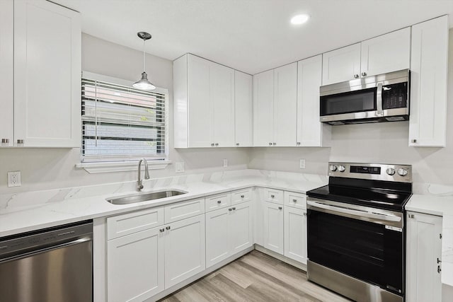 kitchen featuring light stone countertops, light wood-style flooring, stainless steel appliances, white cabinets, and a sink