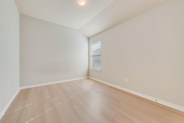 spare room with lofted ceiling, light wood-type flooring, and baseboards