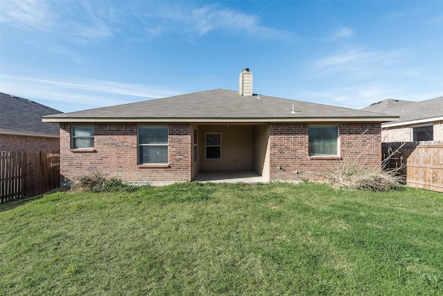 rear view of house featuring a chimney, a fenced backyard, brick siding, a patio area, and a lawn