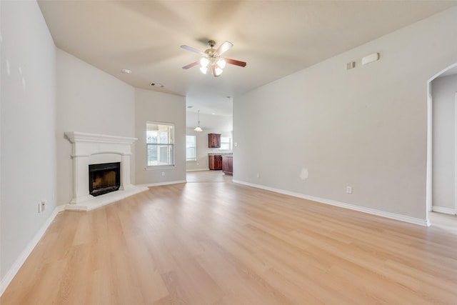 unfurnished living room featuring arched walkways, light wood finished floors, a fireplace with raised hearth, visible vents, and a ceiling fan