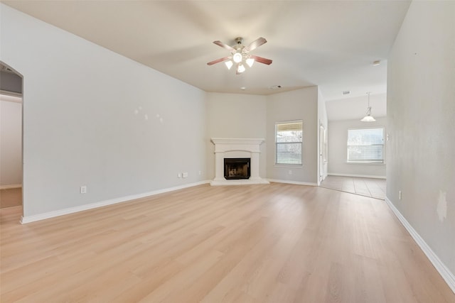 unfurnished living room with a fireplace with raised hearth, a ceiling fan, light wood-style flooring, and baseboards