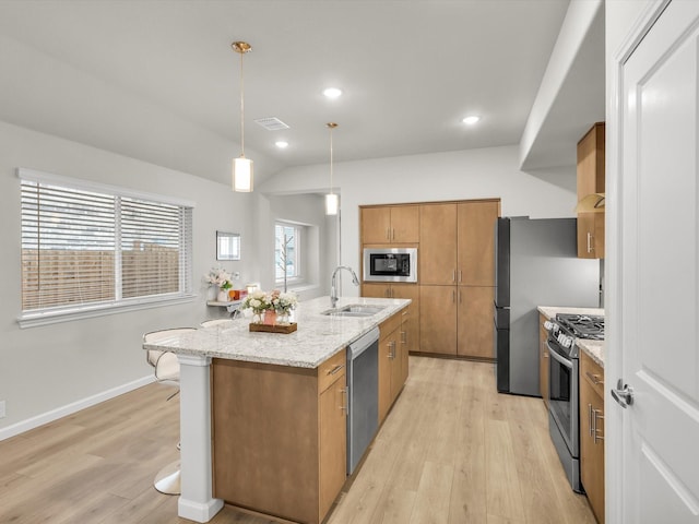 kitchen featuring a sink, stainless steel appliances, light wood finished floors, a kitchen island with sink, and brown cabinetry