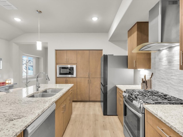 kitchen with light wood finished floors, light stone countertops, a sink, wall chimney exhaust hood, and appliances with stainless steel finishes