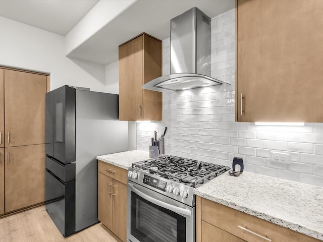 kitchen featuring light stone counters, stainless steel appliances, light wood finished floors, and wall chimney exhaust hood
