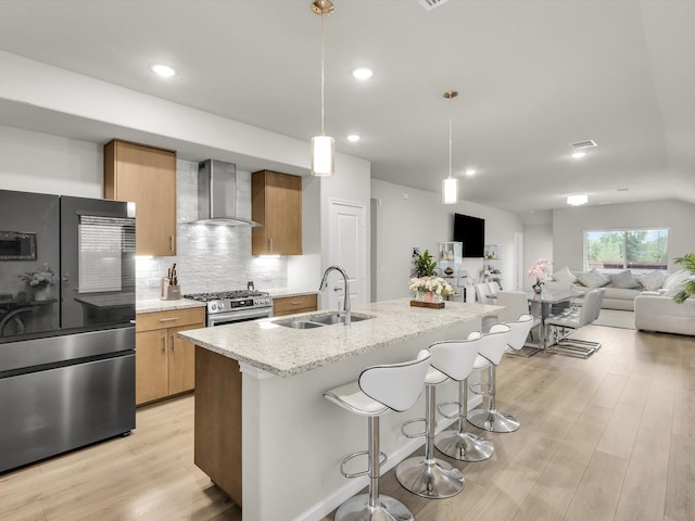 kitchen with light wood finished floors, a sink, decorative backsplash, wall chimney exhaust hood, and appliances with stainless steel finishes