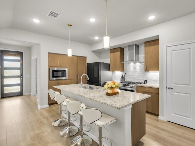 kitchen with a sink, freestanding refrigerator, built in microwave, gas stove, and wall chimney exhaust hood