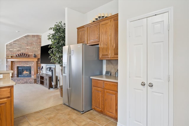 kitchen featuring light tile patterned floors, stainless steel fridge, brown cabinetry, light carpet, and light countertops