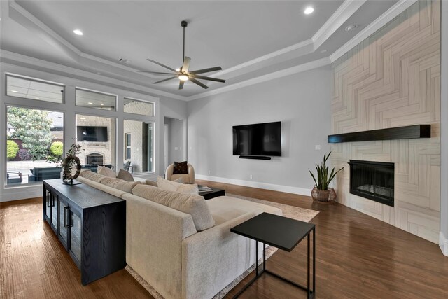 living area with a large fireplace, ceiling fan, dark wood-style flooring, and a raised ceiling