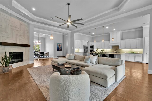 living area featuring crown molding, a tray ceiling, and ceiling fan with notable chandelier