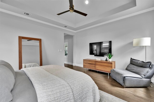 bedroom with a ceiling fan, visible vents, crown molding, wood finished floors, and a tray ceiling