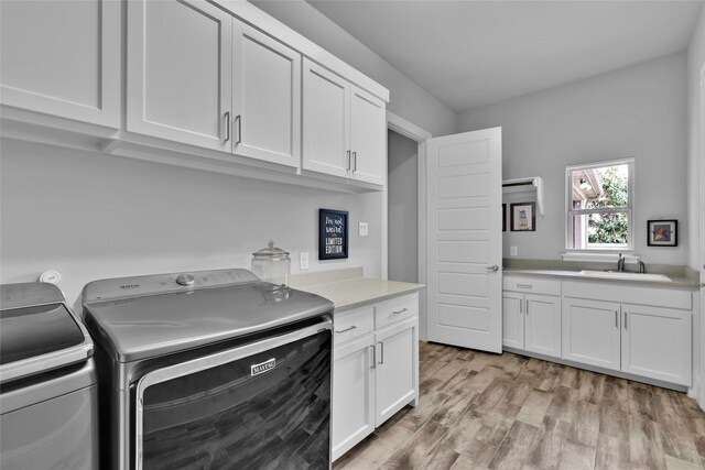 laundry room featuring cabinet space, washer and clothes dryer, a sink, and light wood finished floors