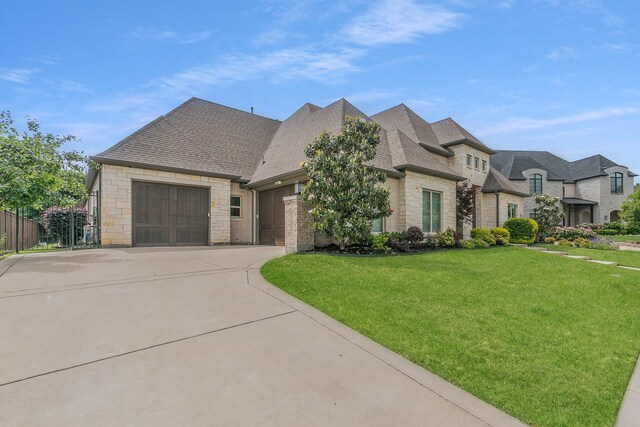 french country inspired facade featuring roof with shingles, a garage, a front lawn, concrete driveway, and stone siding