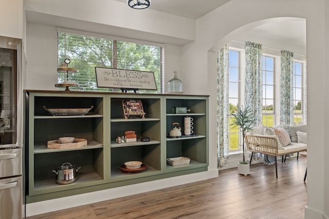 interior space with arched walkways, a healthy amount of sunlight, and wood finished floors
