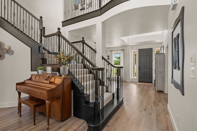 foyer featuring baseboards, light wood-style floors, stairs, and a high ceiling