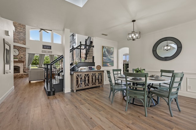 dining room featuring stairway, arched walkways, an inviting chandelier, a brick fireplace, and wood finished floors