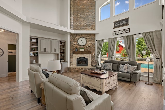 living room with a brick fireplace, a towering ceiling, plenty of natural light, and light wood-style floors