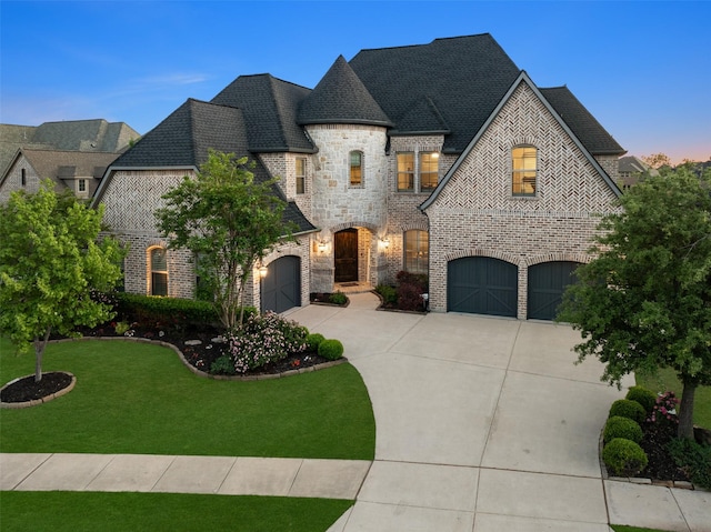 french country home featuring driveway, a front yard, a garage, brick siding, and stone siding