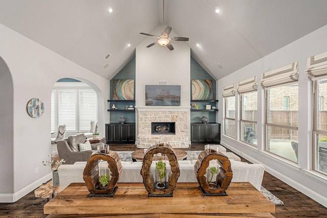 living area featuring ceiling fan, a fireplace, arched walkways, baseboards, and wood finished floors
