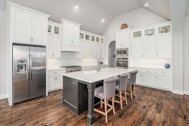 kitchen with a kitchen island with sink, light countertops, white cabinetry, appliances with stainless steel finishes, and backsplash