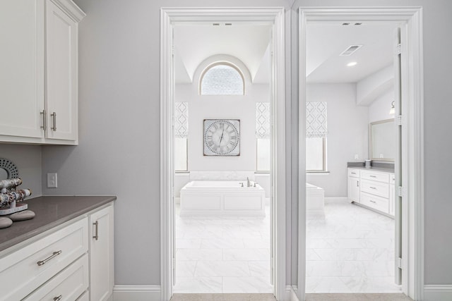 bathroom with a garden tub, visible vents, vanity, marble finish floor, and a wealth of natural light