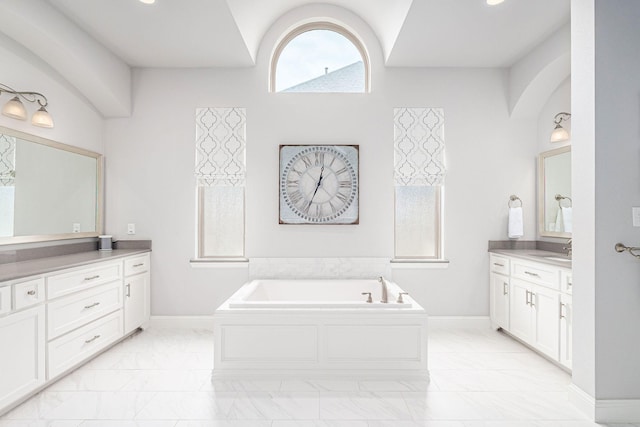 bathroom featuring a garden tub, two vanities, a sink, baseboards, and marble finish floor